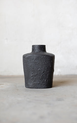 Black textured vase on a light gray surface with a white background