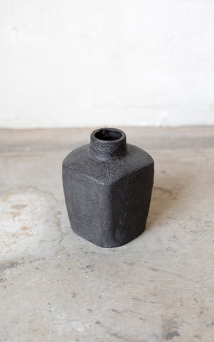 Black ceramic vase on a light gray surface with a white background
