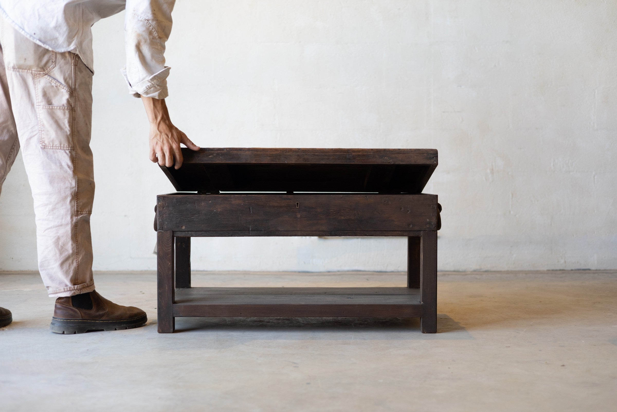 Person lifting opening top to reveal storage compartment in British colonial teak coffee table in a minimalistic room.