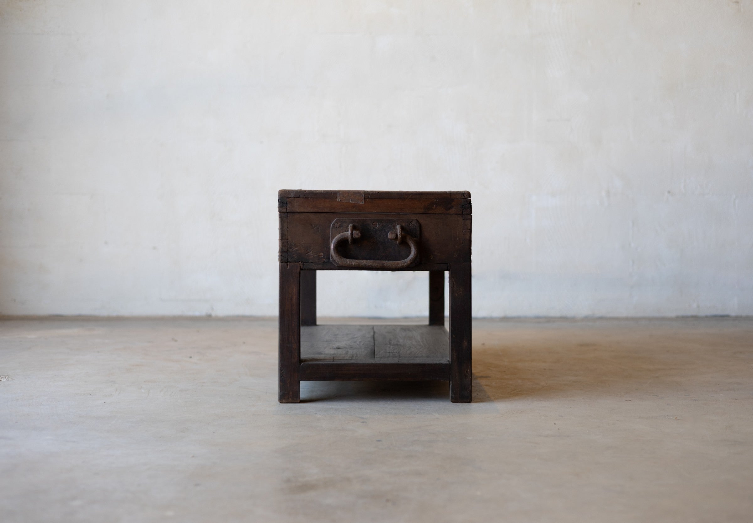 Side of vintage teak wood coffee table with an iron handle on a neutral background.