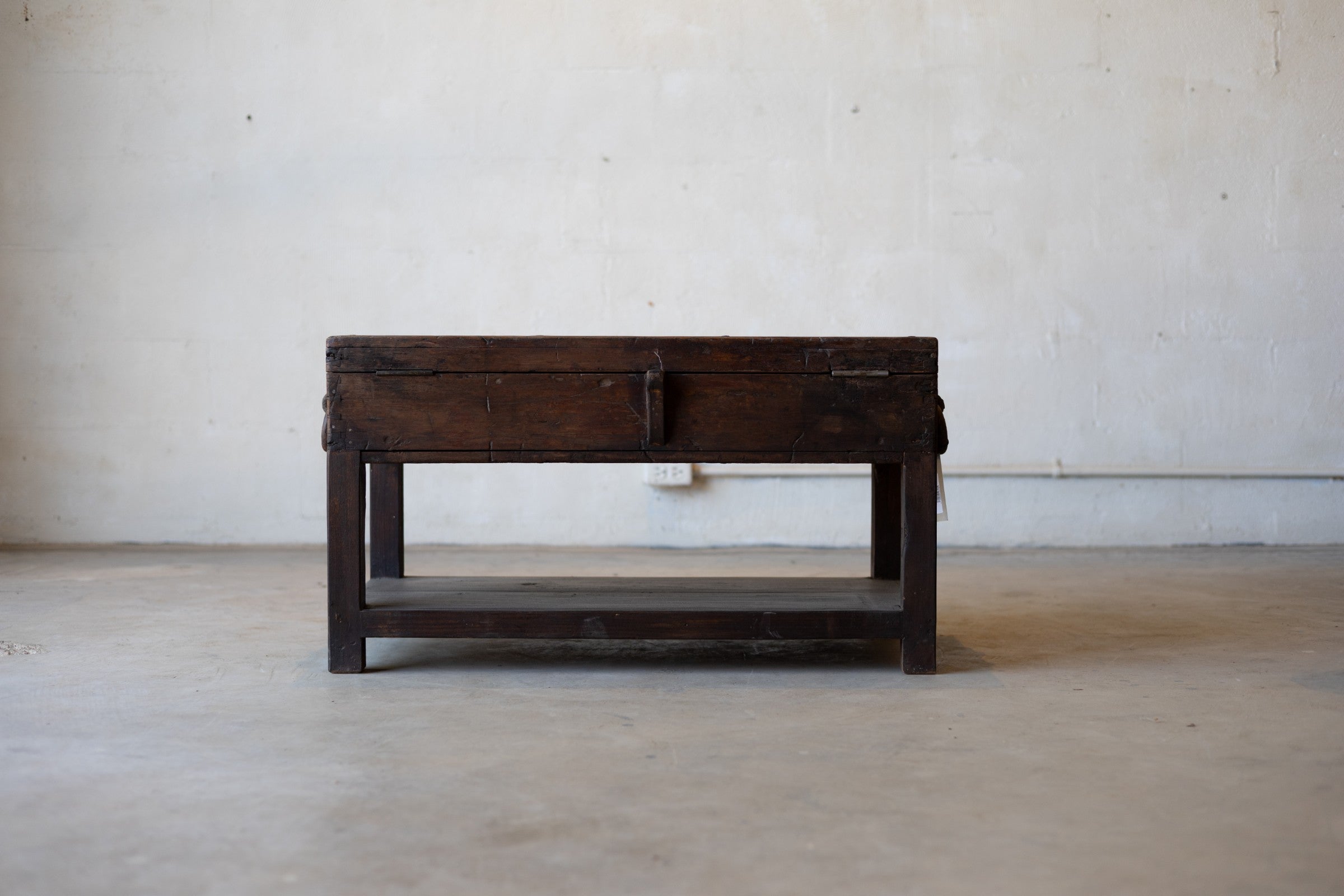 Back of vintage teak wood coffee table with an iron handle on a neutral background.