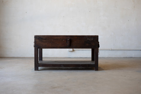 Back of vintage teak wood coffee table with an iron handle on a neutral background.