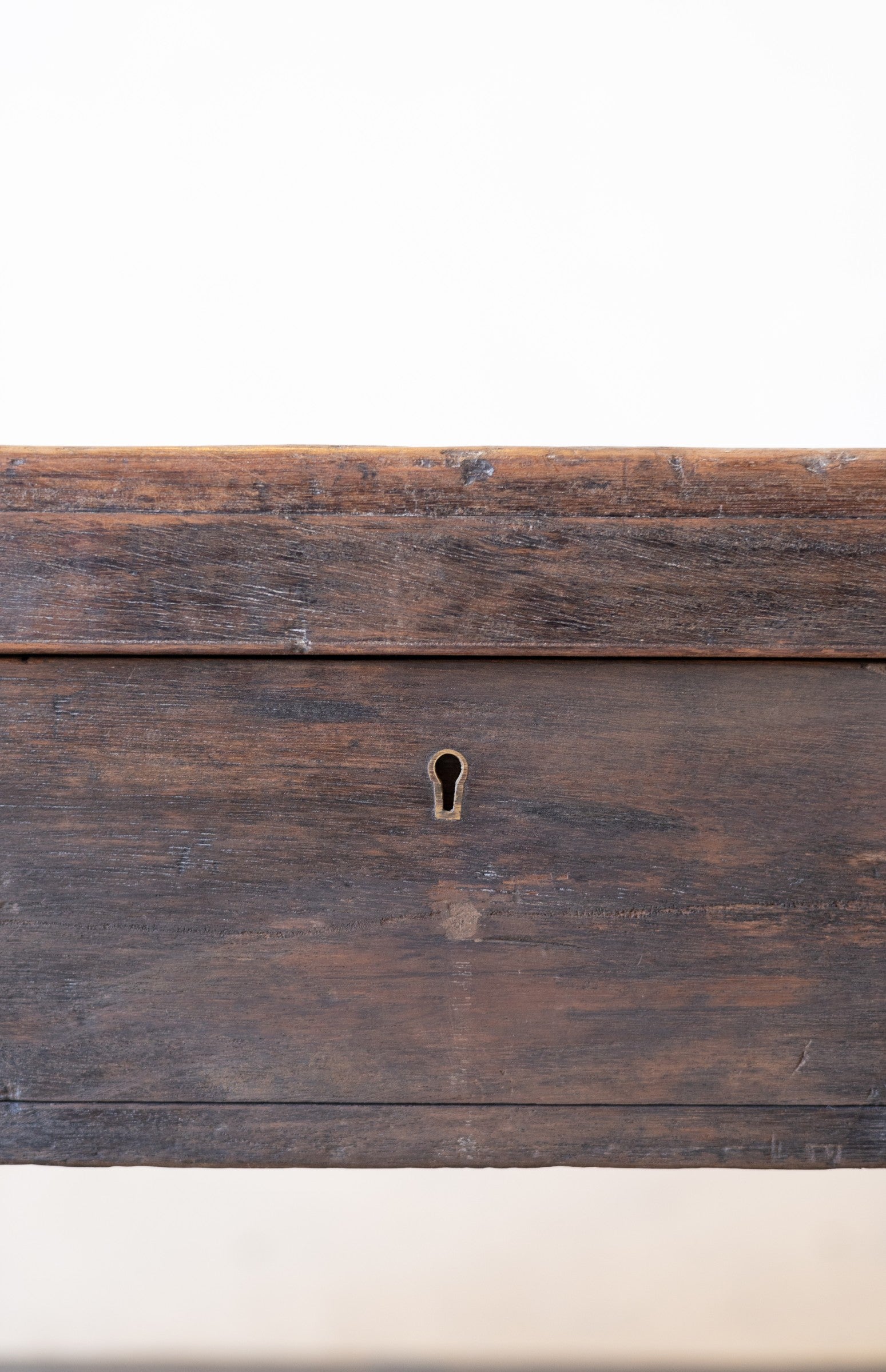 Close up of keyhole of storage compartment of vintage teak wood coffee table with an iron handle on a neutral background.