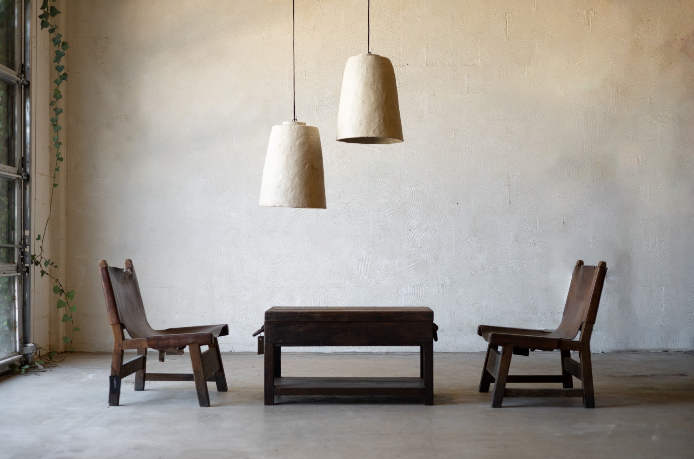 Two wooden chairs and a vintage coffee table with pendant lights in a minimalistic room.