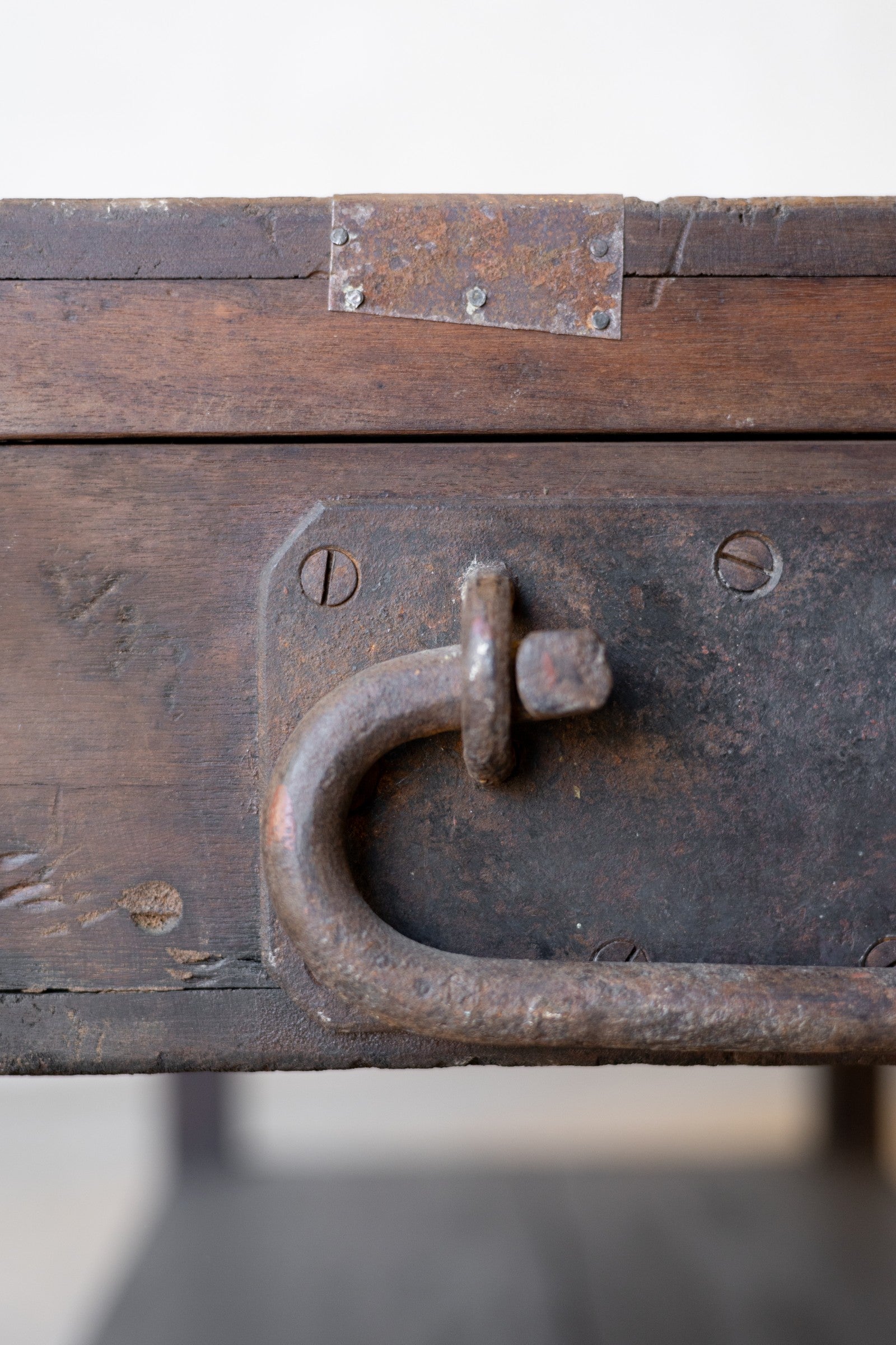 Close up of the side of a vintage teak wood coffee table with an iron handle on a neutral background.