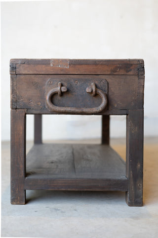 Side of vintage teak wood coffee table with an iron handle on a neutral background.