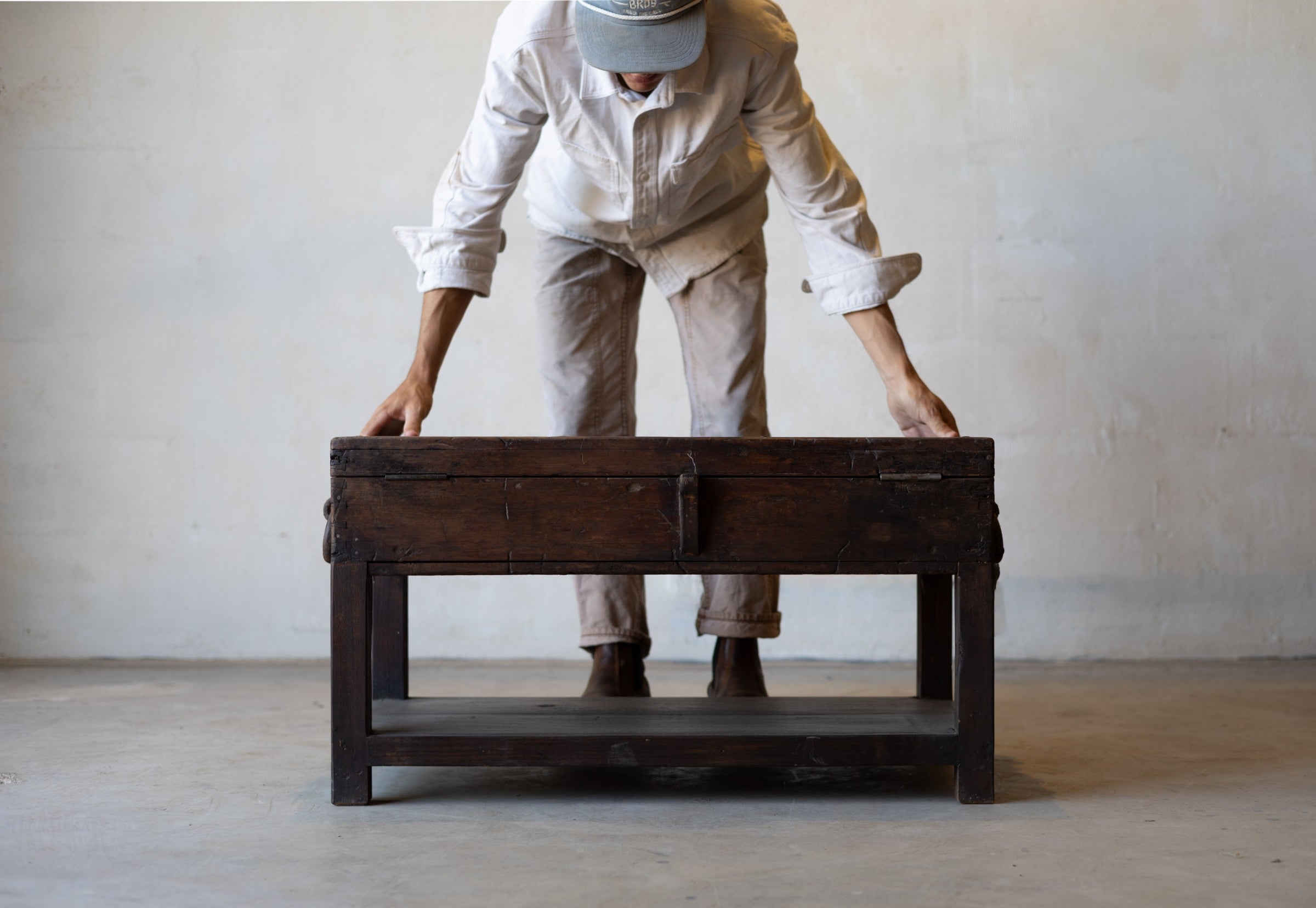 Man standing with arms outstretched over vintage teak wood coffee table with an iron handle on a neutral background.