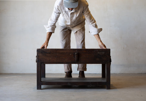 Man standing with arms outstretched over vintage teak wood coffee table with an iron handle on a neutral background.