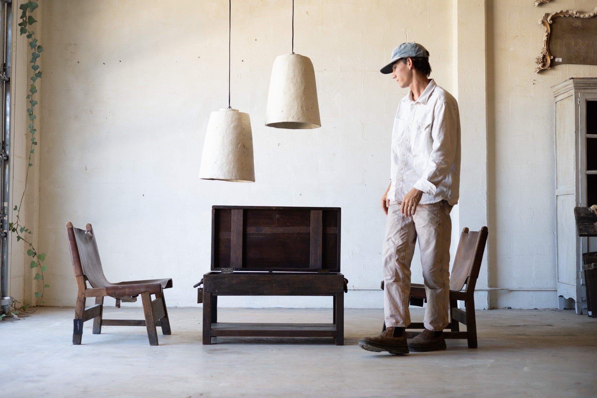 Man sanding next to a British colonial teak coffee table with opening top in a minimalistic room with large windows and pendant lights.