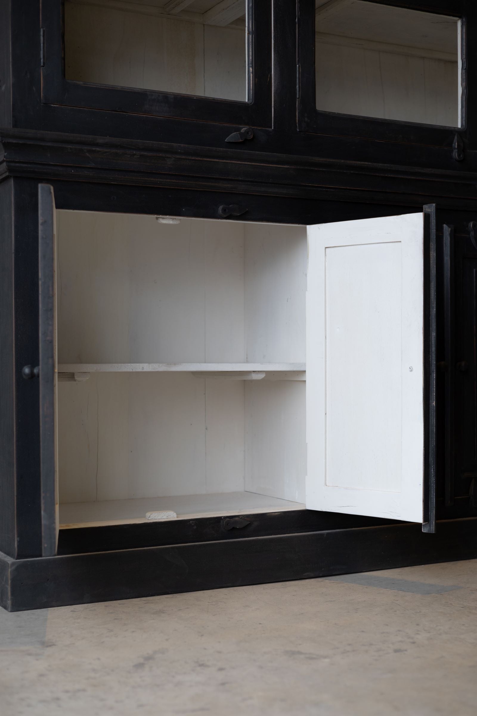 Bottom of black wooden hutch with bottom solid doors open revealing white interior with a shelf making two levels of storage. 