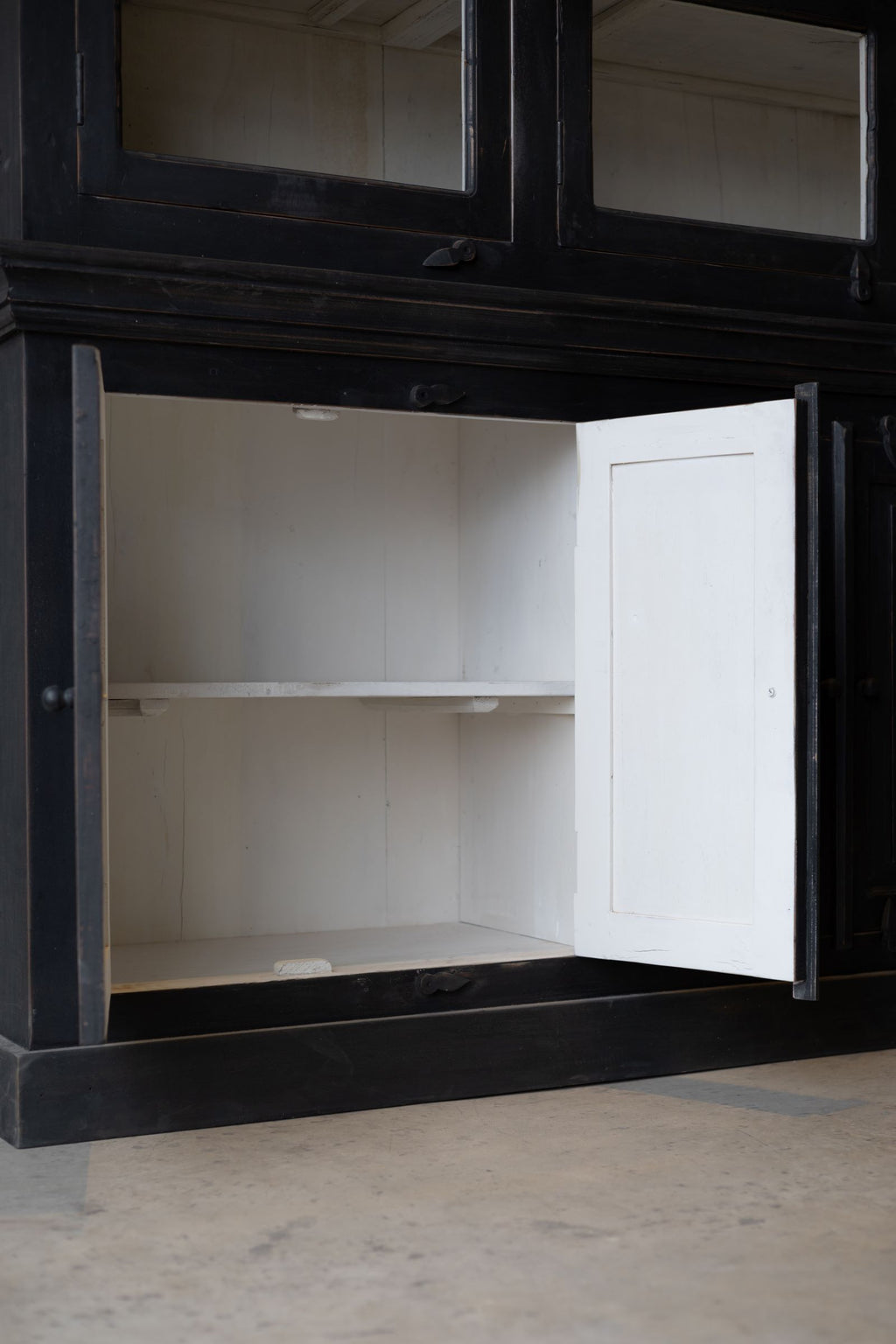 Bottom of black wooden hutch with bottom solid doors open revealing white interior with a shelf making two levels of storage. 