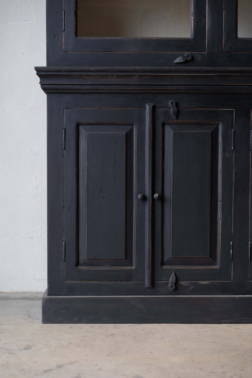 Detail of the lower section of a black wooden hutch, showing two paneled cabinet doors with round knobs and decorative metal latches.
