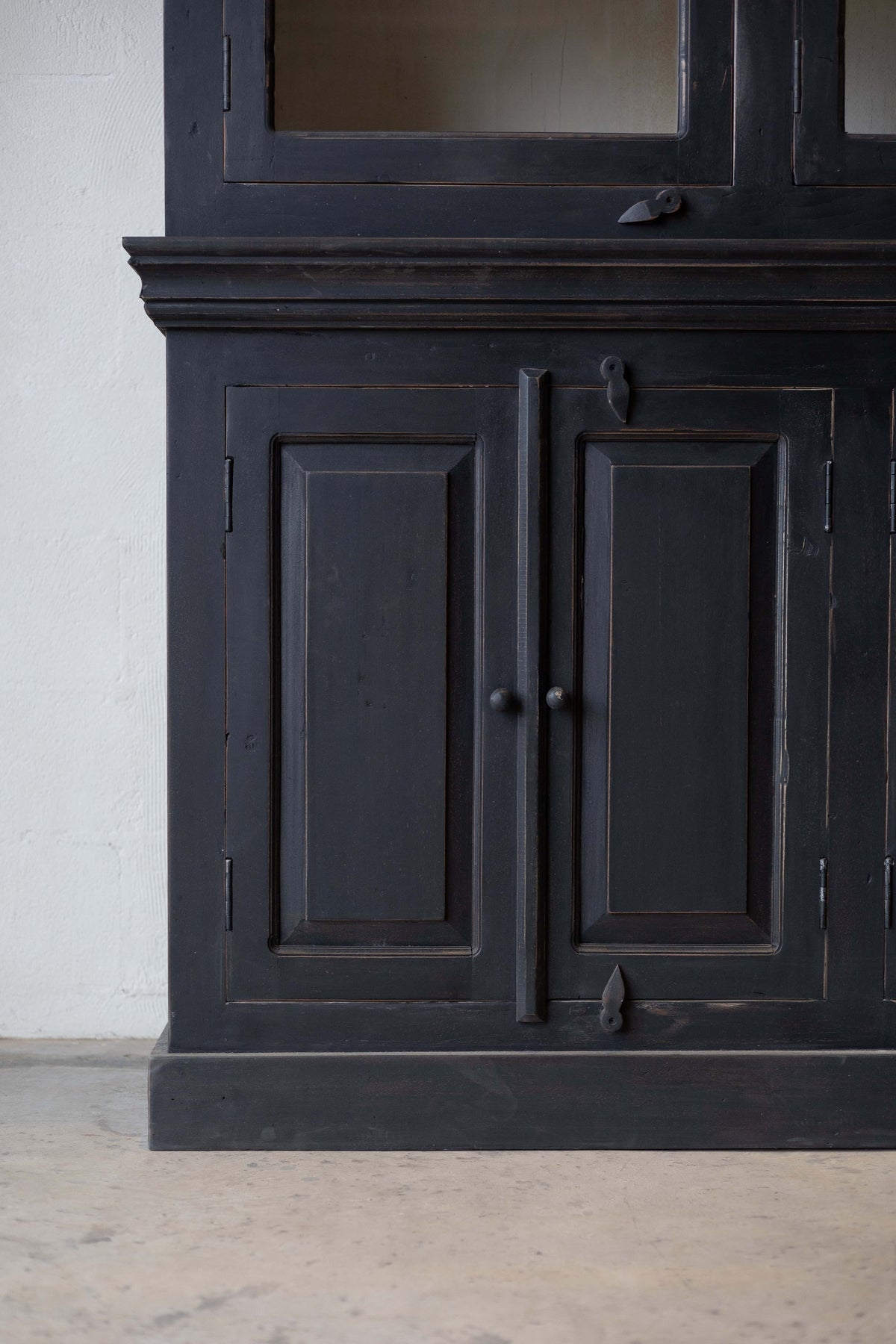 Detail of the lower section of a black wooden hutch, showing two paneled cabinet doors with round knobs and decorative metal latches.