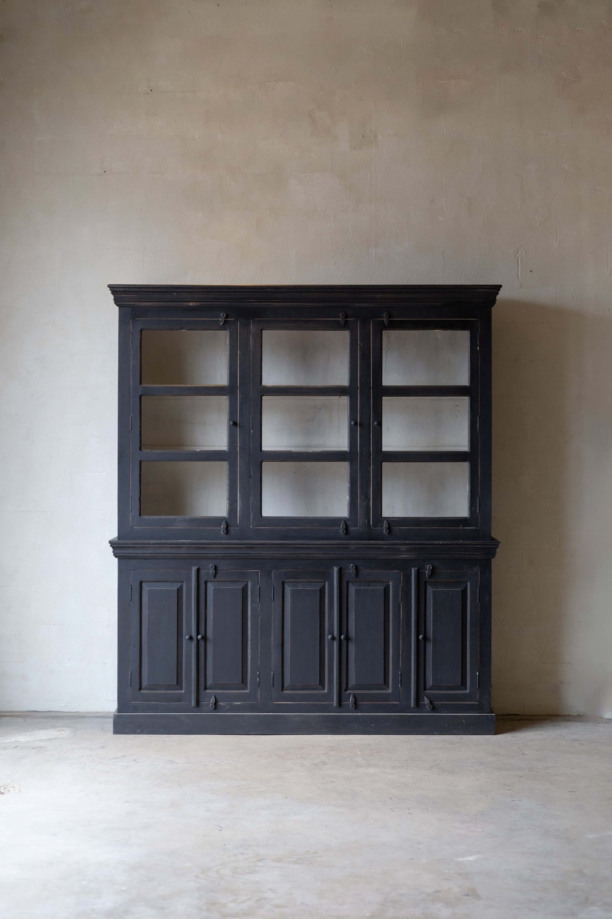 Vertical image of black wooden hutch with three glass doors on top and five closed storage cabinets below, set against a neutral wall. Main image