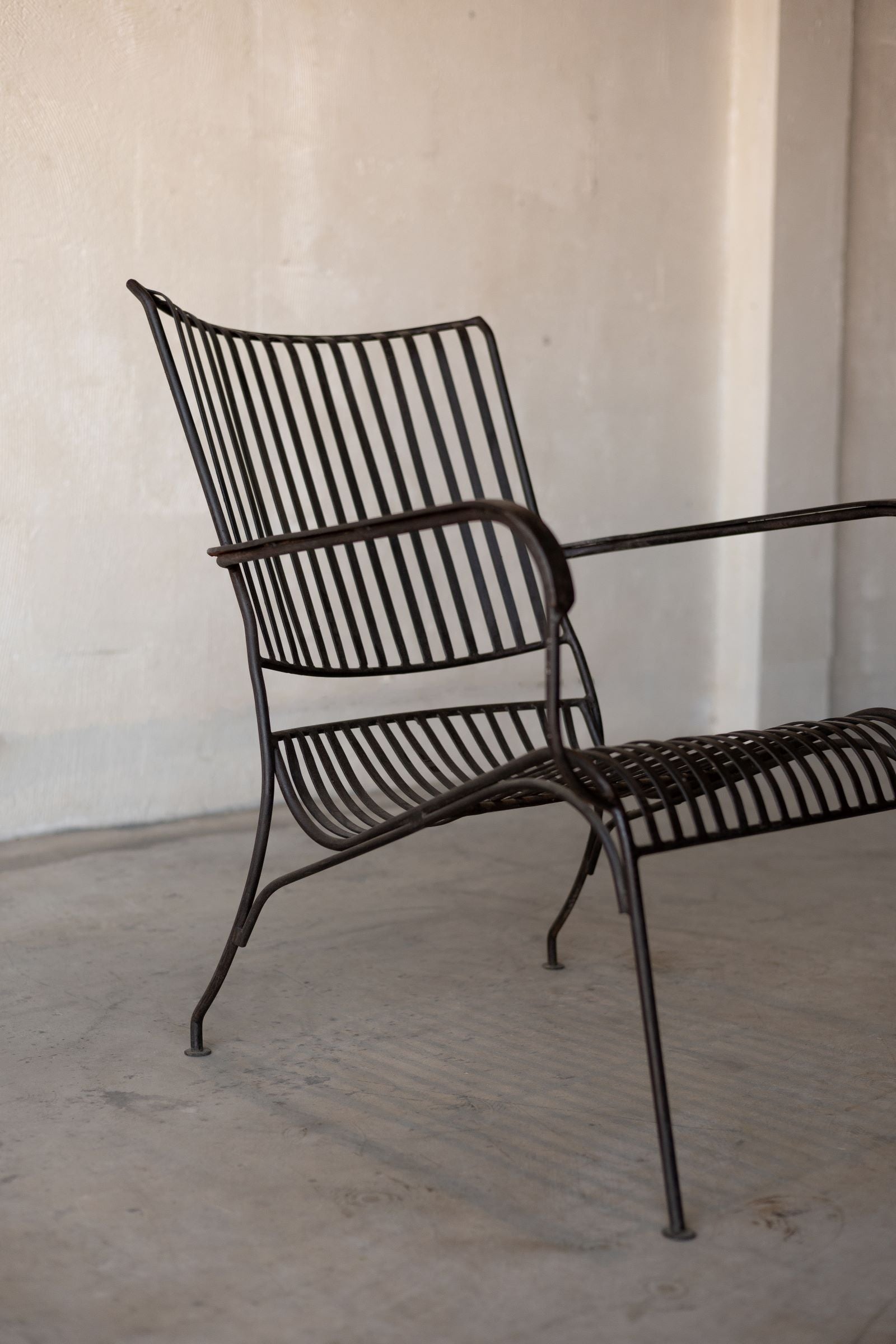 Side angle view of black iron lounge chair with vertical back slats, armrests, and curved seat.