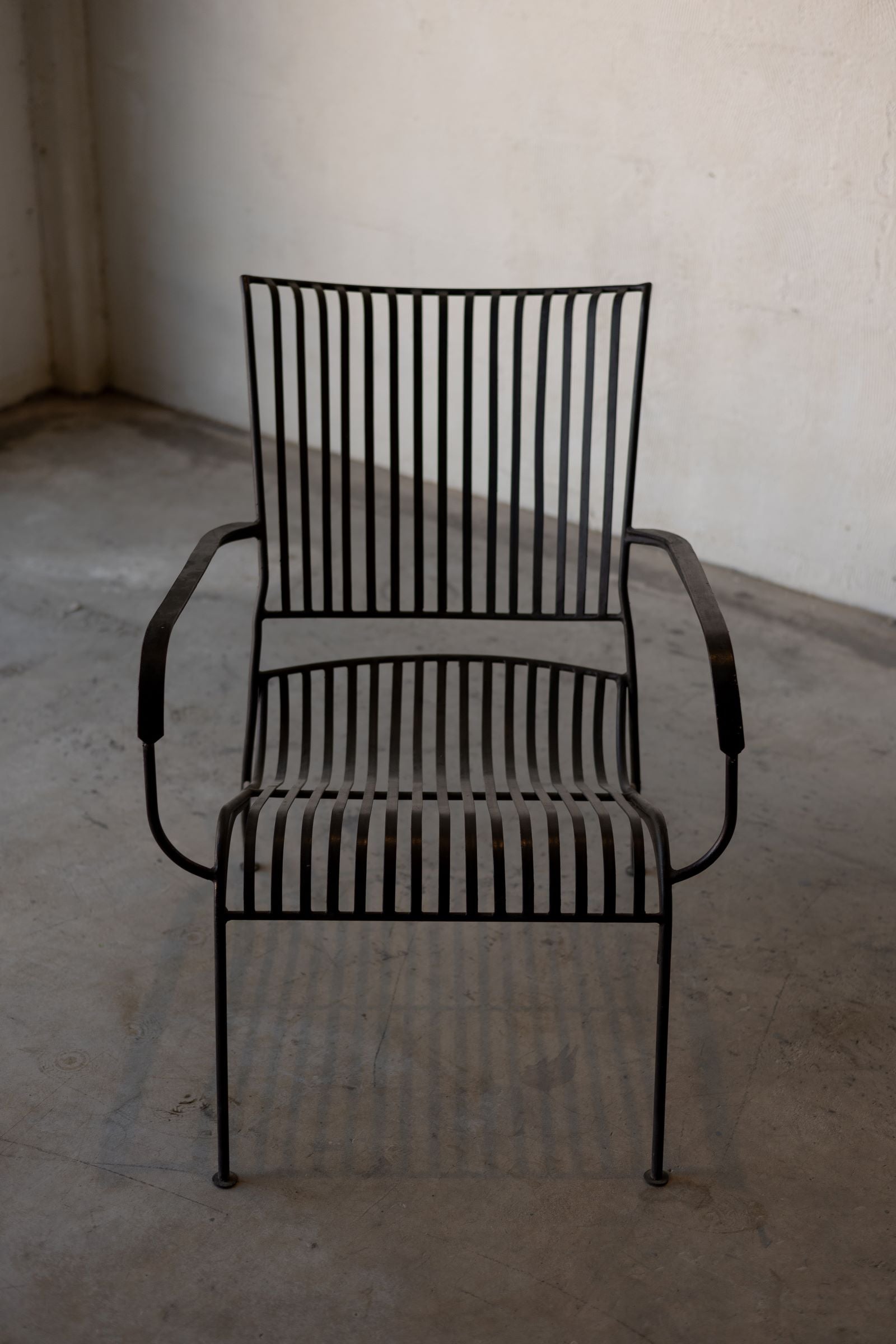 Frontal view of black iron lounge chair with vertical back slats, armrests, and curved seat.