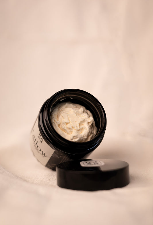 Open jar of tallow skin cream with a beige background.