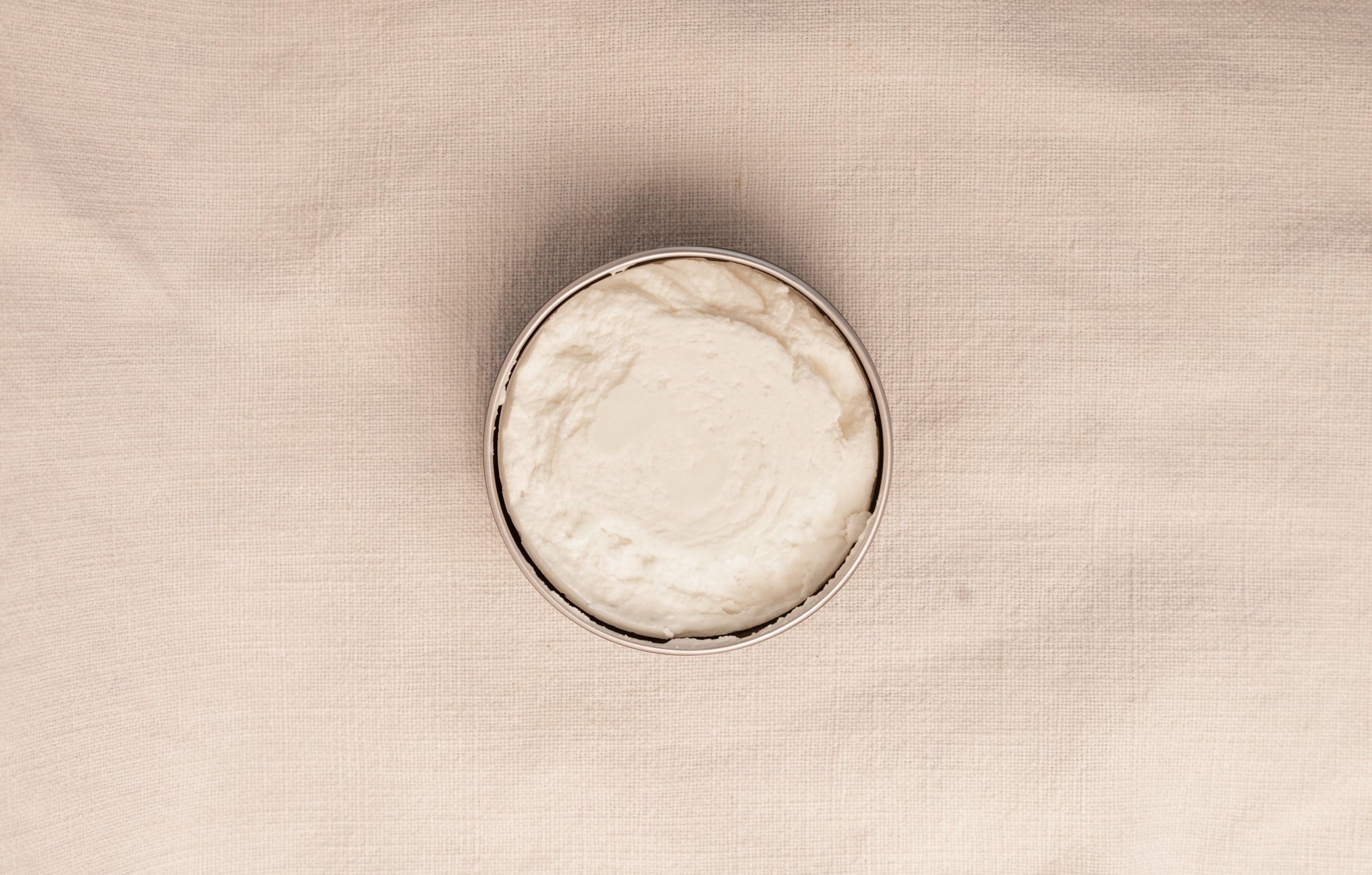 Open jar of tallow body creme on a beige background viewed from the top.