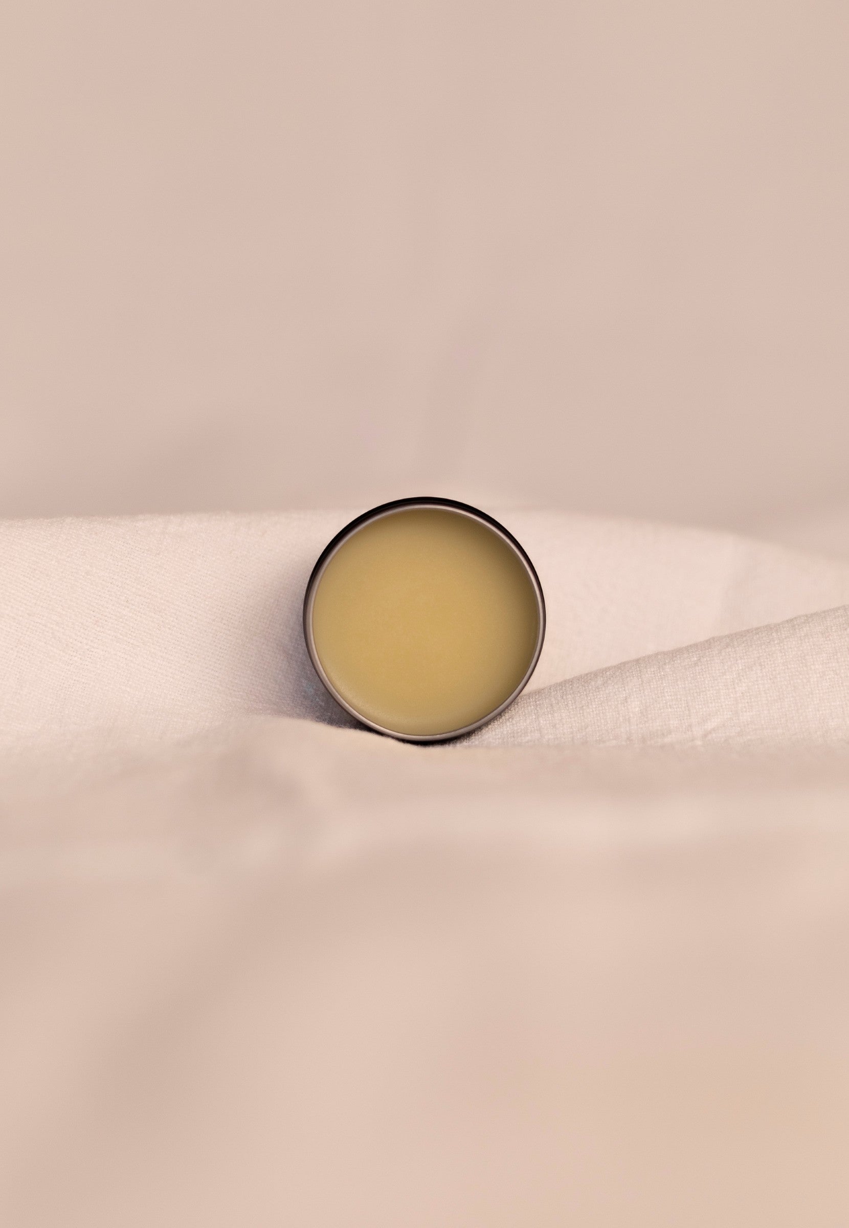 Small round open container of beef tallow balm on a beige fabric background.