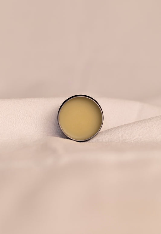 Small round open container of beef tallow balm on a beige fabric background.