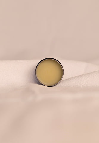Small round open container of beef tallow balm on a beige fabric background.