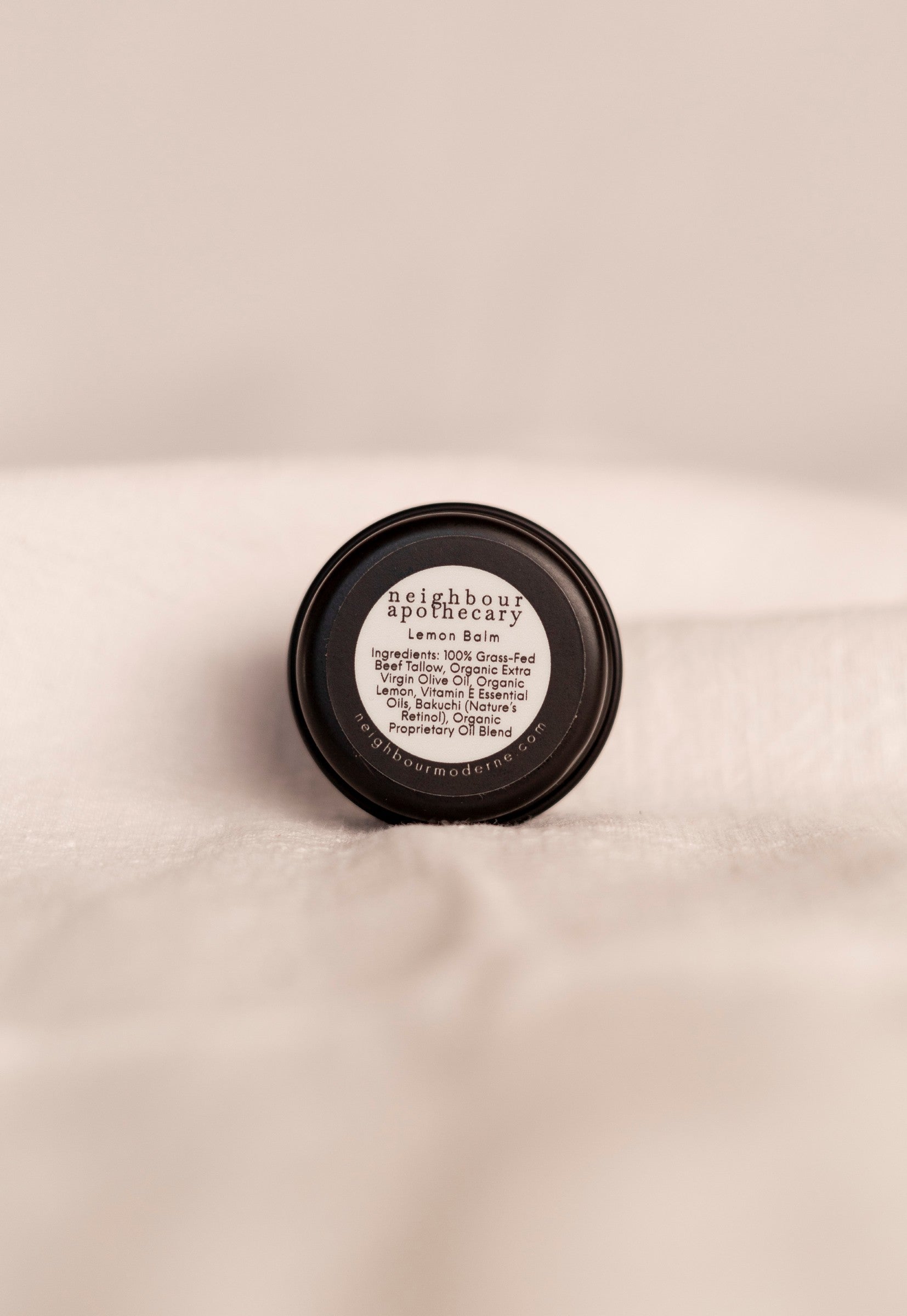 Back of round tin of lemon beef tallow balm with ingredient label on a beige background.