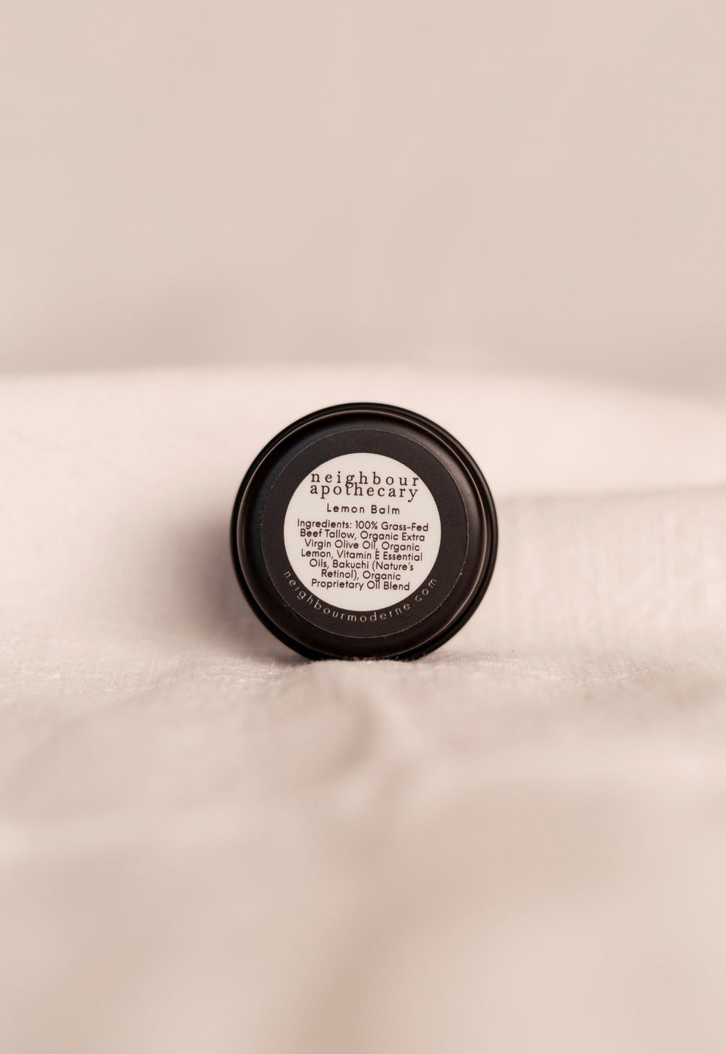 Back of round tin of lemon beef tallow balm with ingredient label on a beige background.