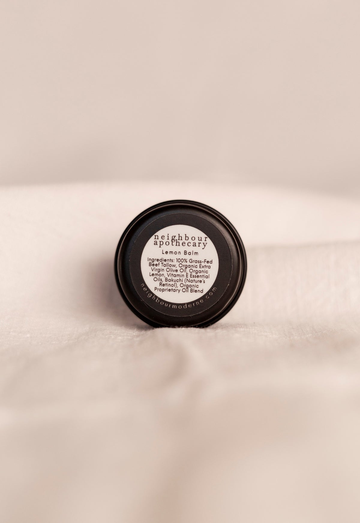 Back of round tin of lemon beef tallow balm with ingredient label on a beige background.
