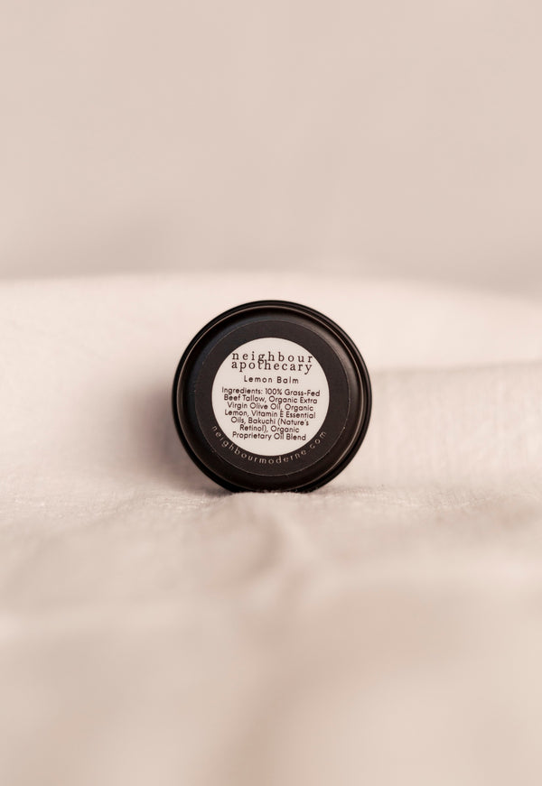 Back of round tin of lemon beef tallow balm with ingredient label on a beige background.