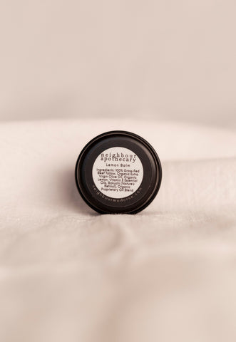 Back of round tin of lemon beef tallow balm with ingredient label on a beige background.