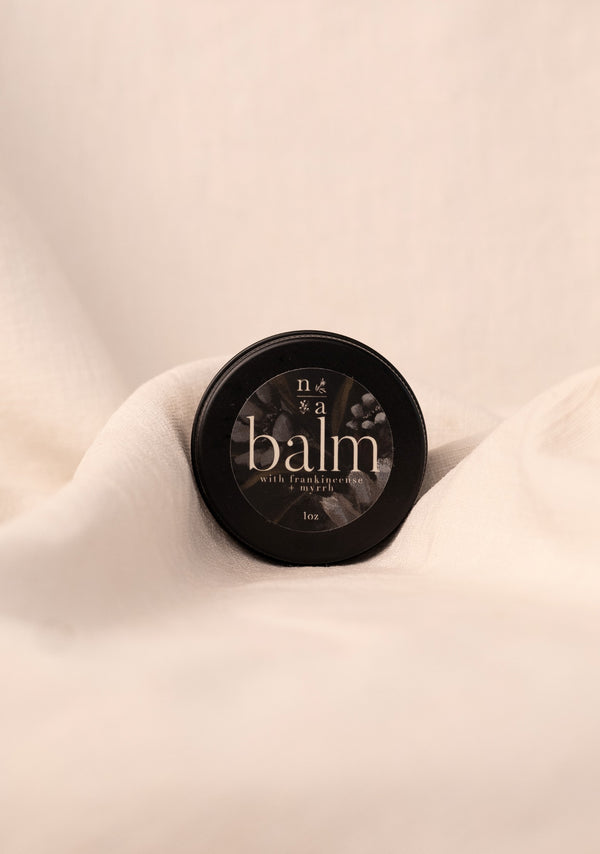 Black container of tallow balm on a beige fabric background.