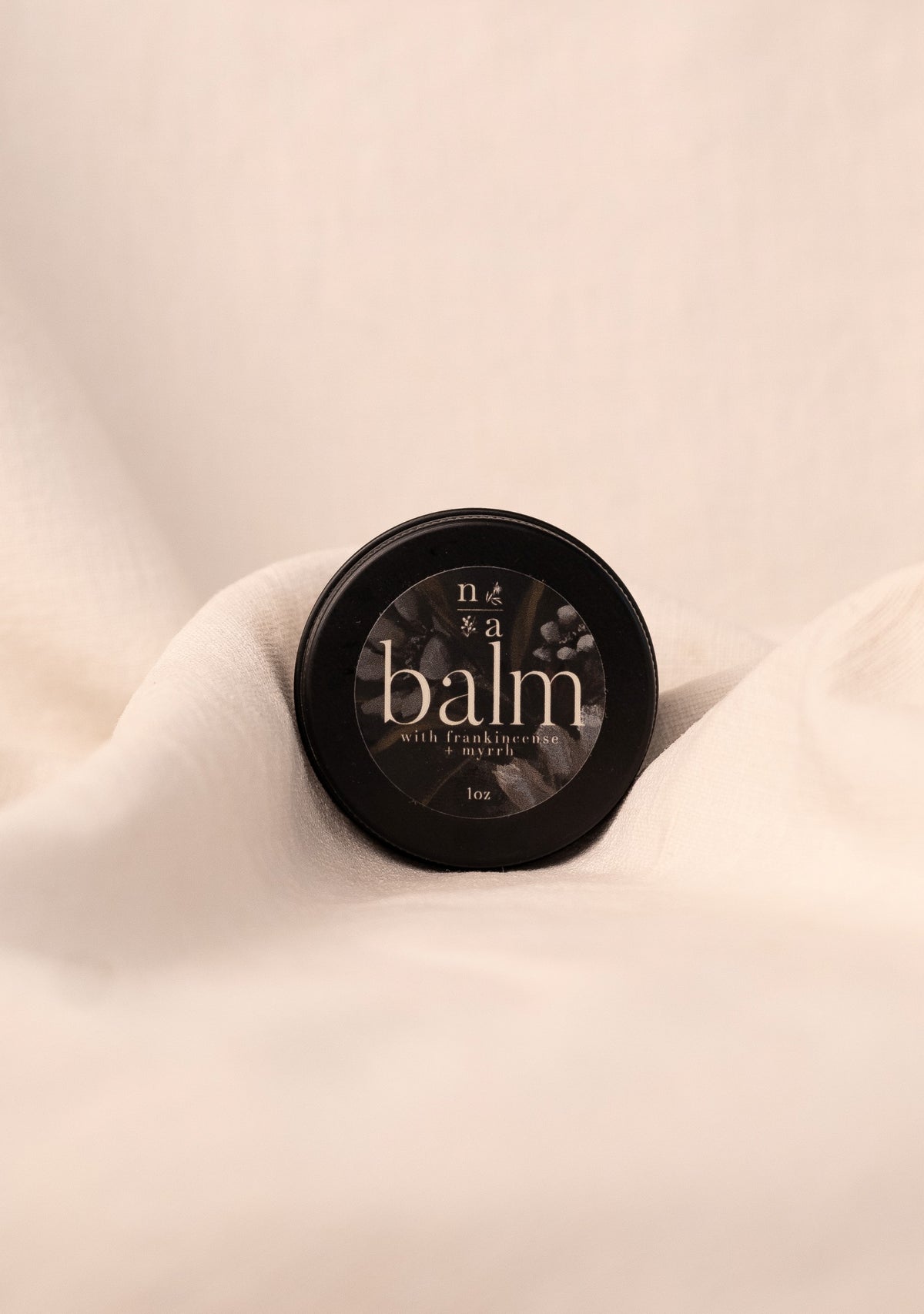 Black container of tallow balm on a beige fabric background.