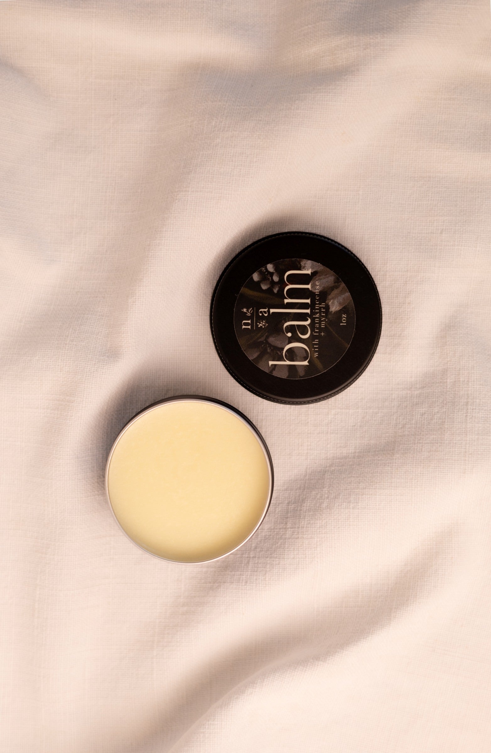 Open container of tallow balm with lid on a soft fabric background.