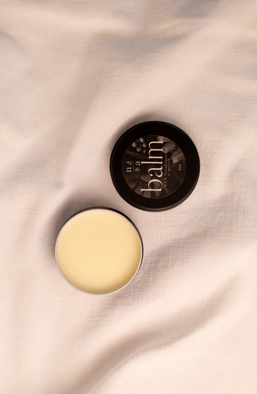 Open container of tallow balm with lid on a soft fabric background.