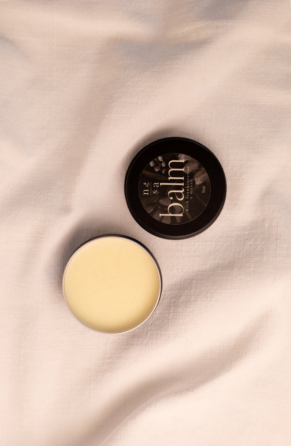Open container of tallow balm with lid on a soft fabric background.