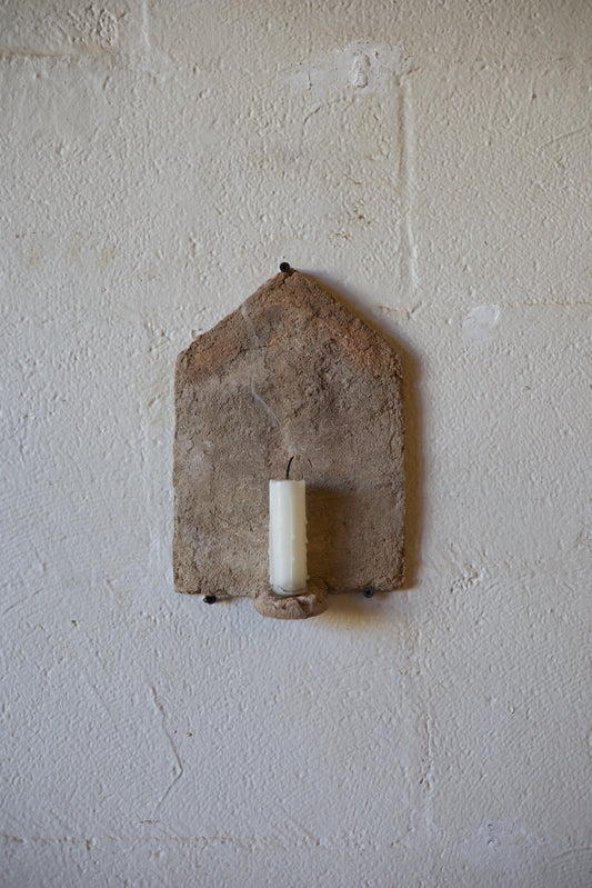 Small stone candle holder on a textured beige surface with an unlight white candle.