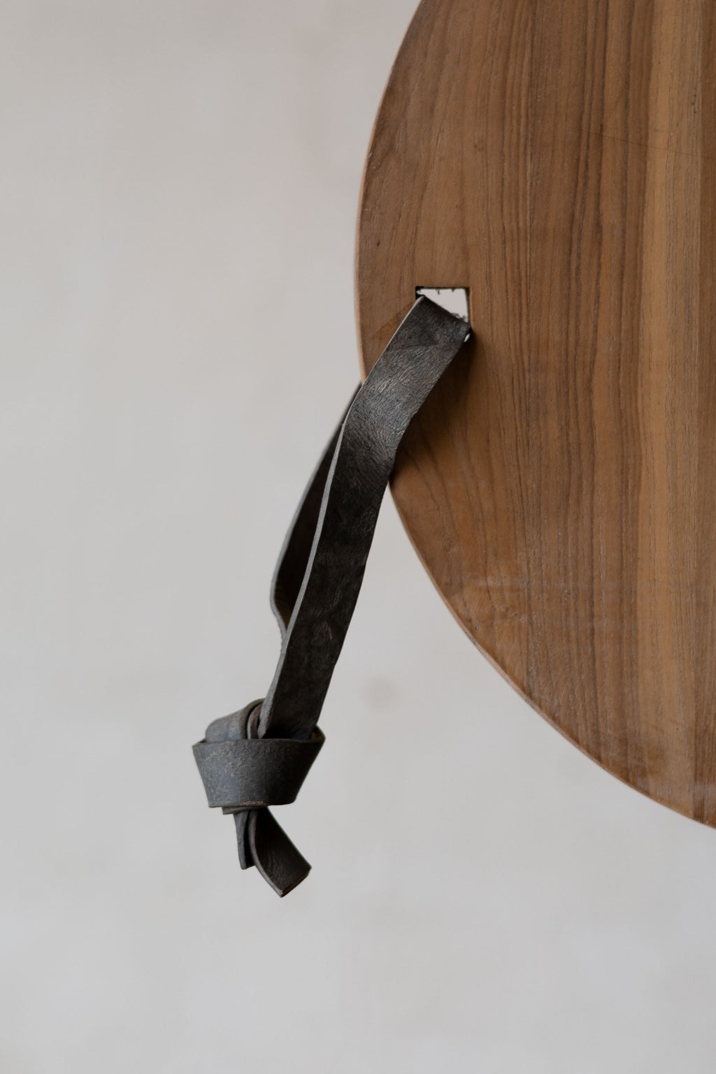 Side of round teak wood cheese board with leather strap. 