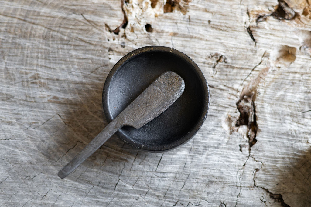 Overhead view of round black iron salt holder with butter knife on top. 