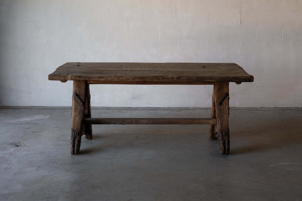 A rustic, wooden sawhorse dining table with A-frame legs and metal reinforcements