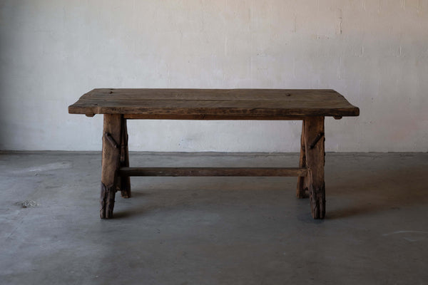 A rustic, wooden sawhorse dining table with A-frame legs and metal reinforcements