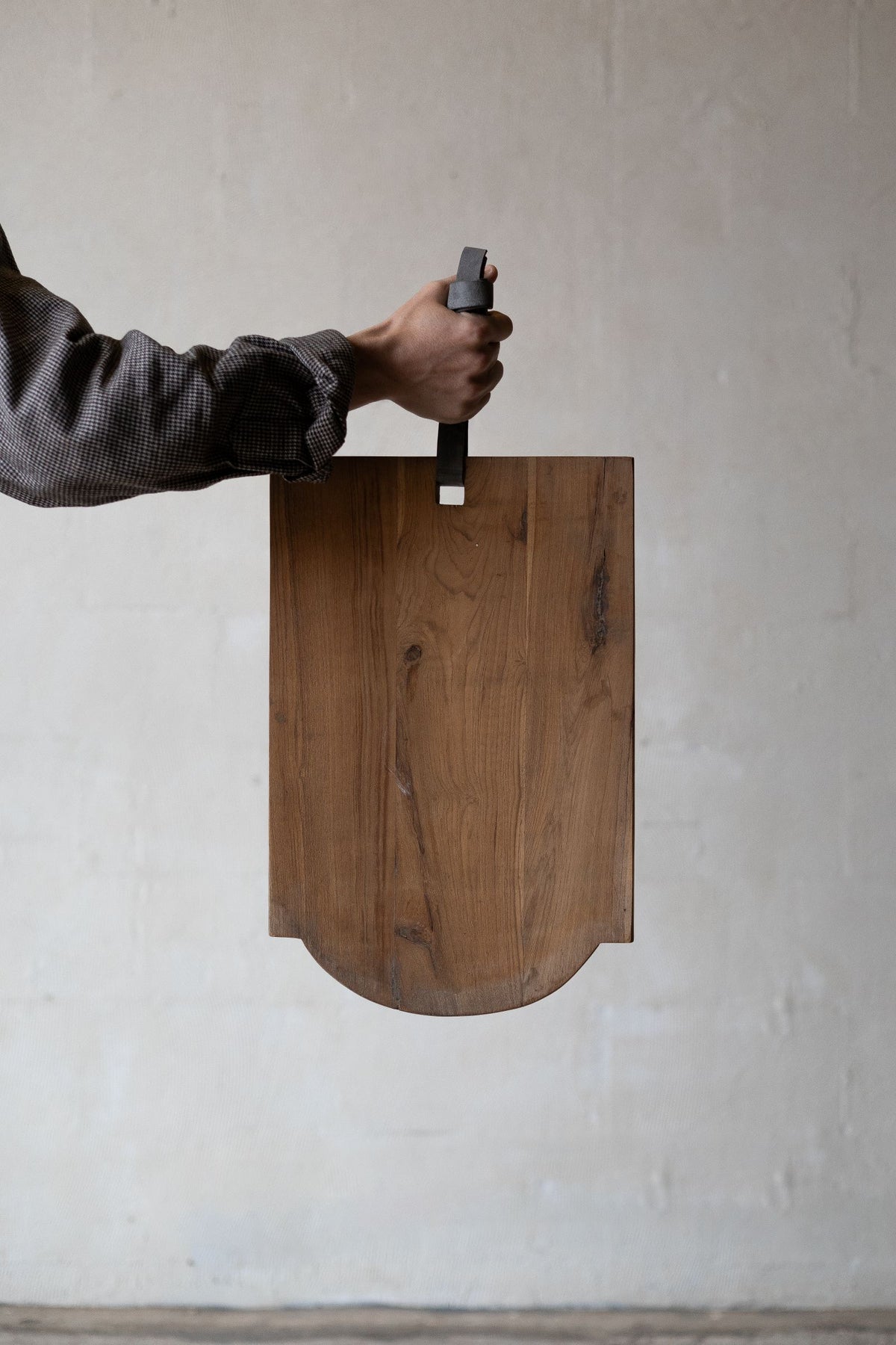 Scalloped teak wood cheese board being held by leather strap.  Main image