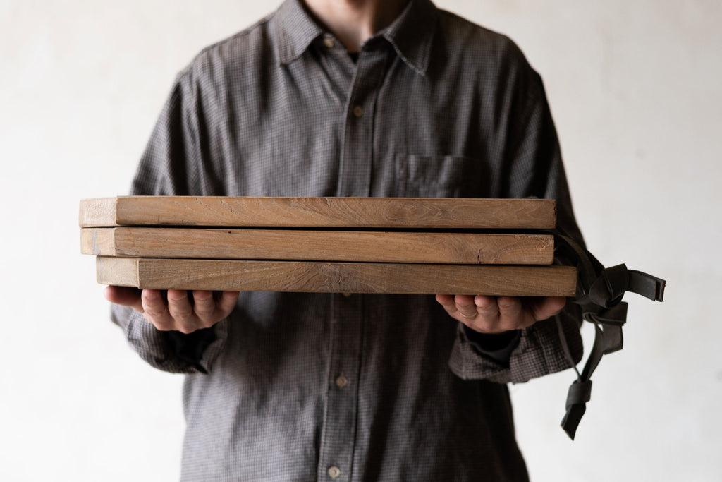 Stack of scalloped teak wood cheese boards being held. 