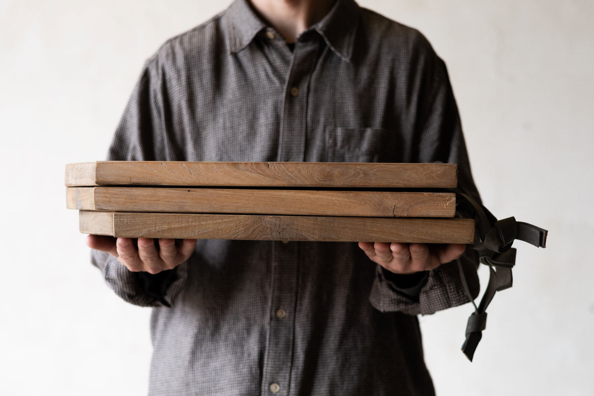 Stack of scalloped teak wood cheese boards being held. 