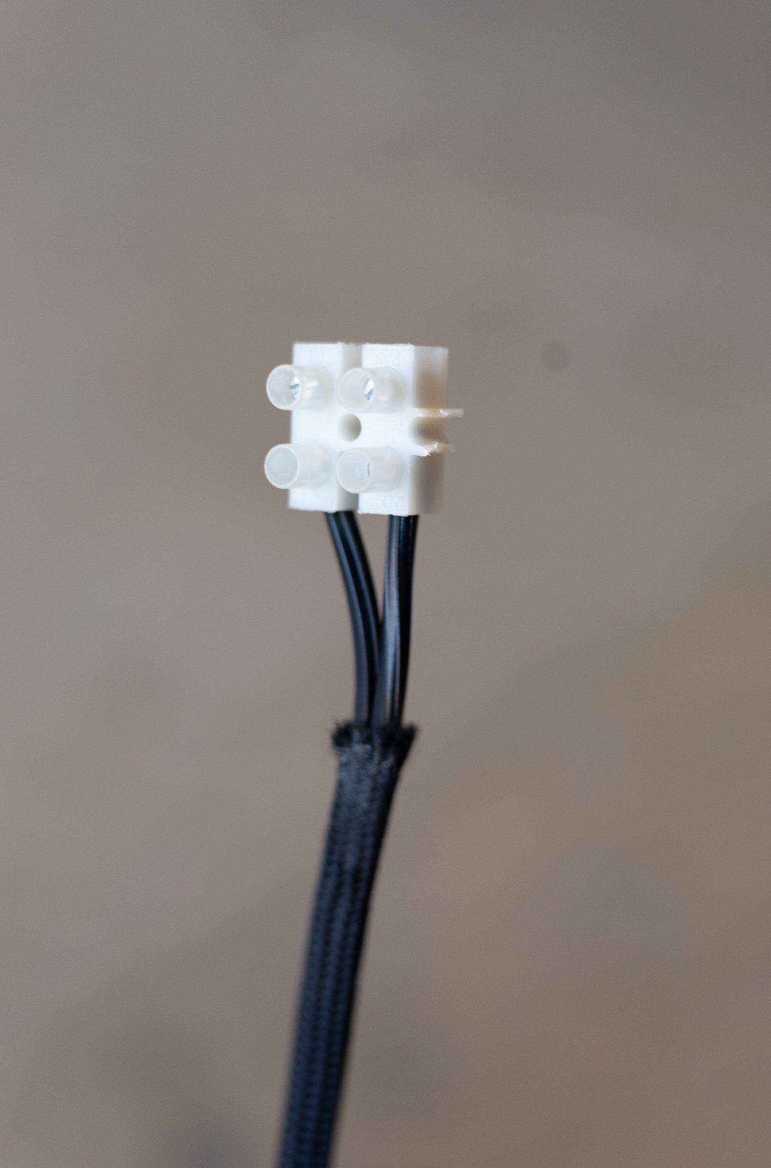 White electronic connector with black wires on a gray background.