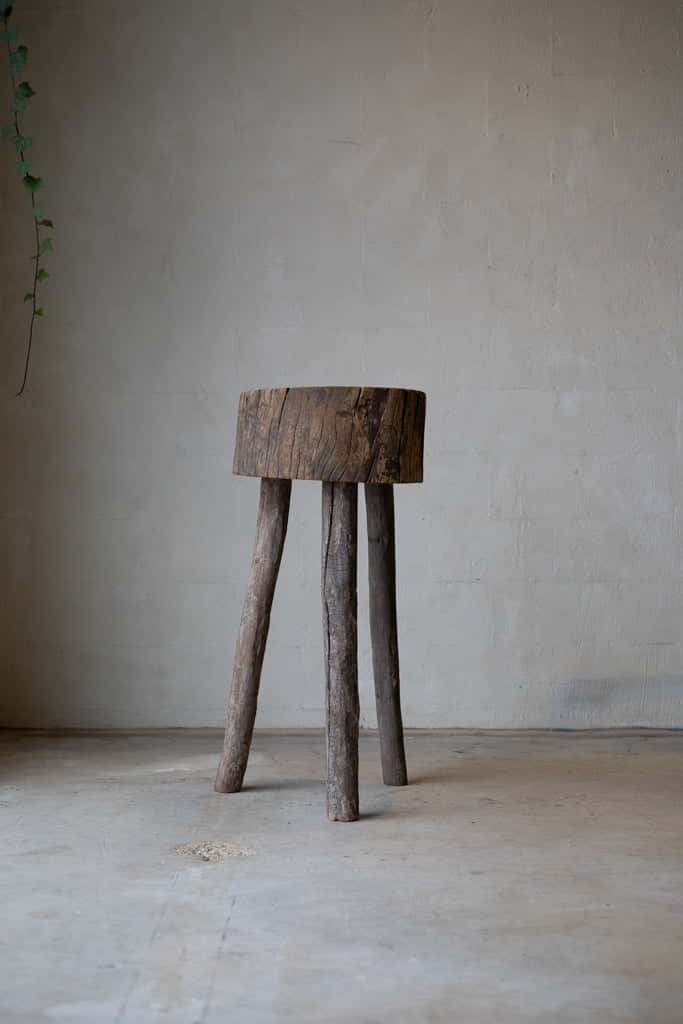 A butcher block table, constructed out of a short stump and three rustic, wood peg legs.