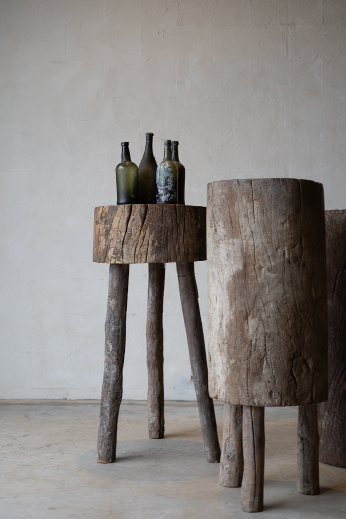 Three tree-trunk tables in French butcher block style: one is a small cylinder with three wood peg legs; one is a long block of trunk with three short legs; one is a tall section of tree trunk. 