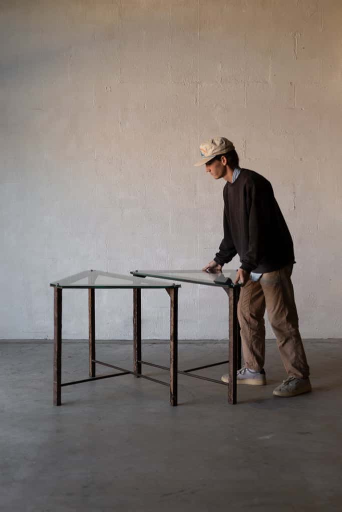 Man pushing triangular table with glass top and iron frame towards the edge of an identical table. Main image