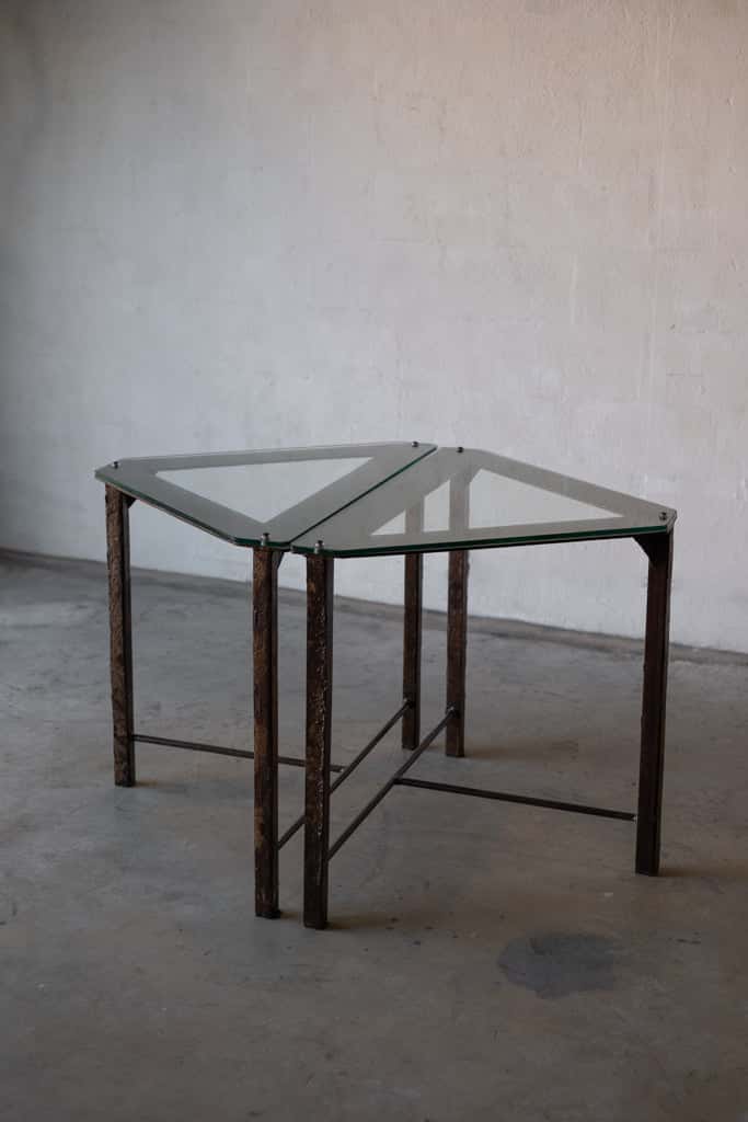 Two triangular side tables with glass tops and industrial iron frames pushed together to create a diamond shape. 