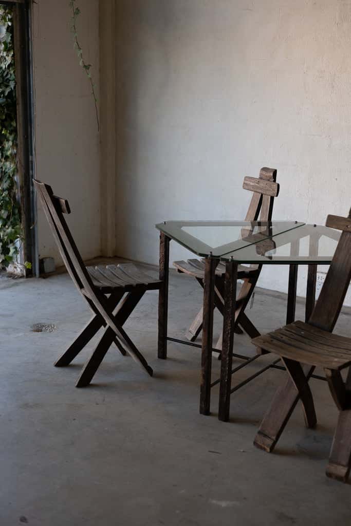 Two triangular glass-top side tables with iron frames surrounded by wooden lounge chairs.