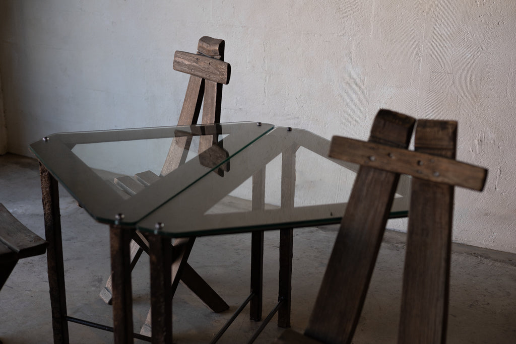 Two triangular glass-top side tables with iron frames surrounded by wooden lounge chairs.